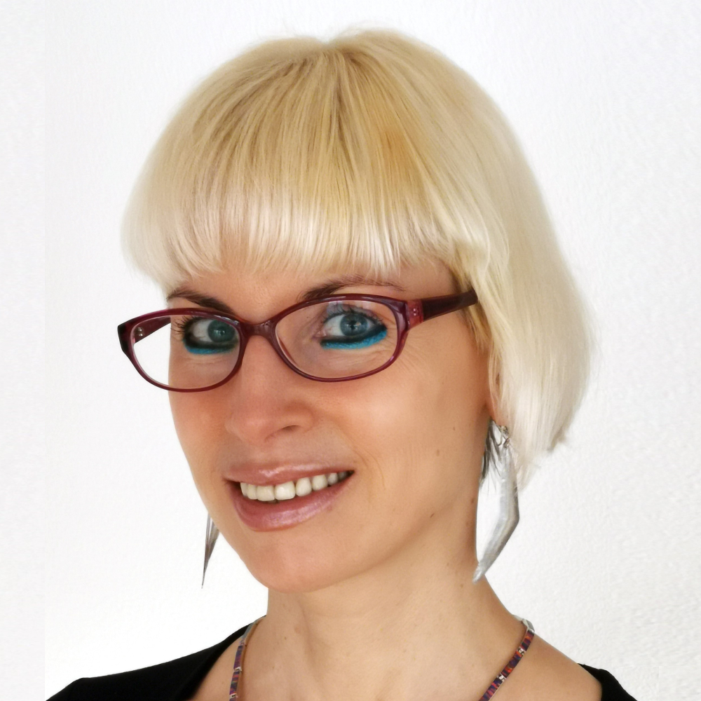 Portrait Prof. Dr. Greta Patzke, weiblich lesbare, hellhäutige Person mit Brille, Ohrringen, Kette und schwarzem Oberteil